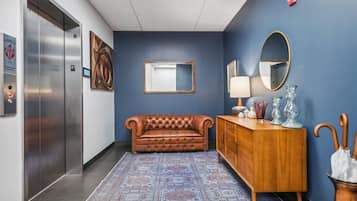 A hallway with a brown leather couch, a wooden dresser with glass vases, and a blue wall with a mirror and artwork.