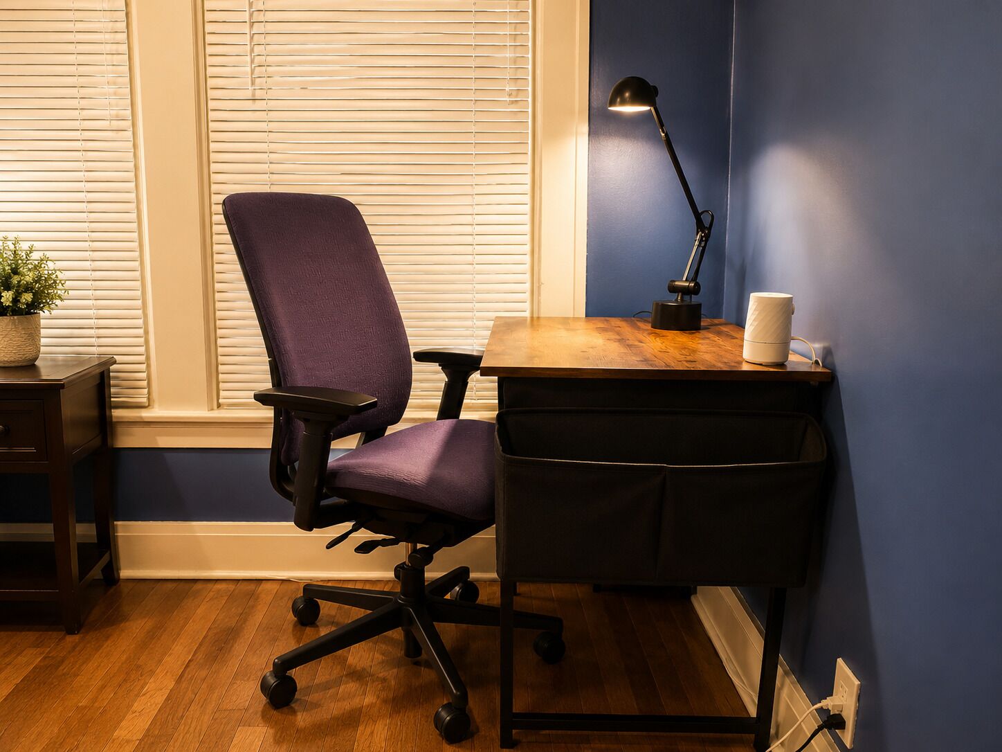 Ein Zimmer mit einem violetten Bürostuhl, einem Holztisch, einer schwarzen Schreibtischlampe und einer weißen Tasse.