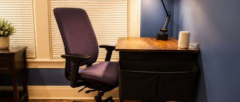 A room with a purple office chair, a wooden desk, a black desk lamp, and a white mug.