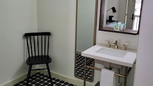 A bathroom with a black and white hexagonal tile floor, a white sink with gold fixtures, a black chair, and a large mirror. - Standard King Room - NKS (Gatlinburg)