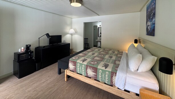 A bedroom with a bed, a desk, a chair, a lamp, a microwave, and a painting on the wall. - Standard King Room - NKS (Gatlinburg)