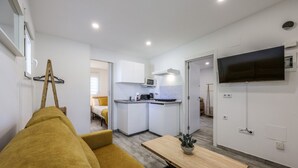 Un espacio habitable compacto con sofá, una pequeña cocina y un televisor montado en la pared.