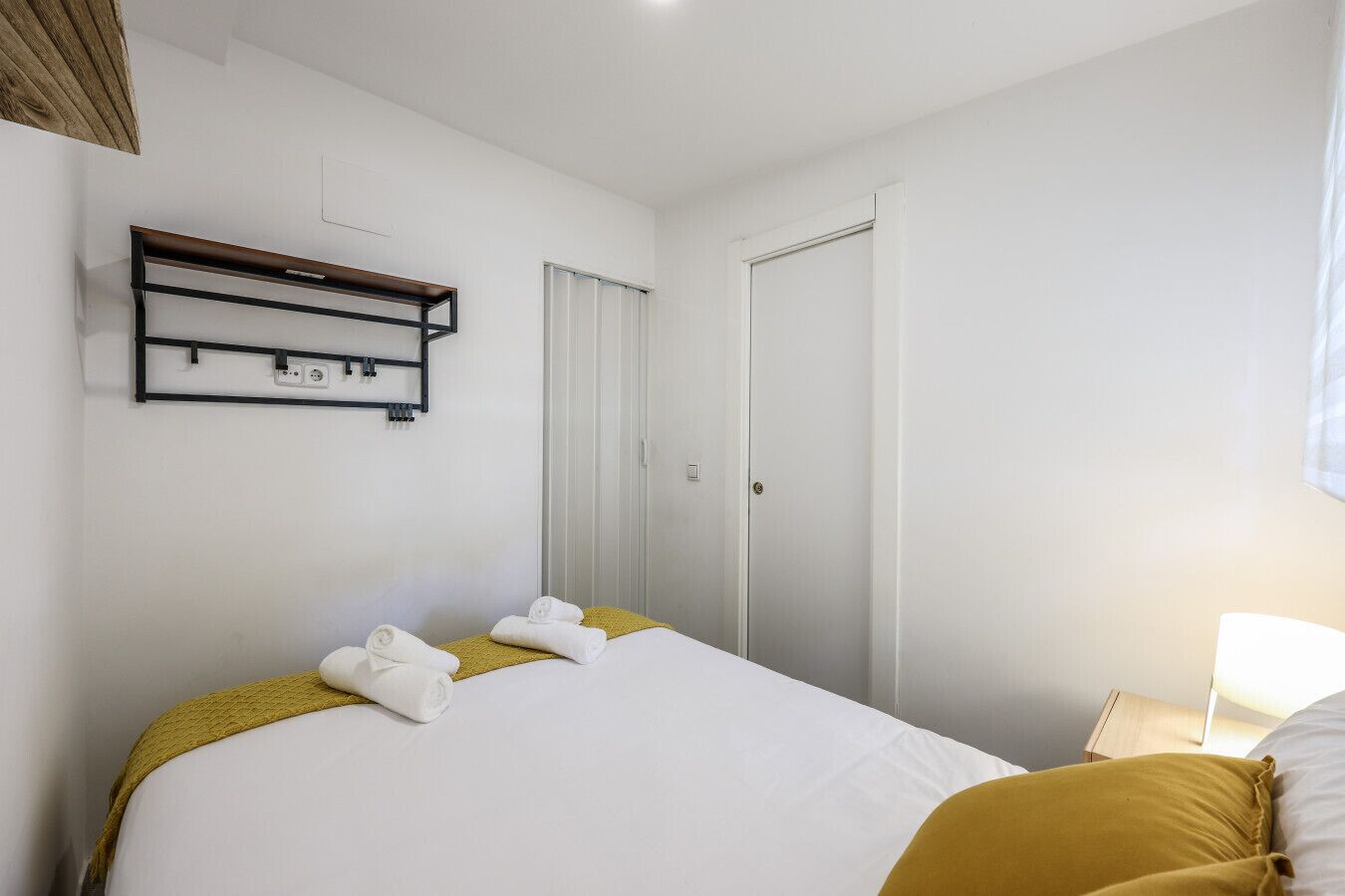 Een hotelkamer met een bed, nachtkastje, lamp en een kledingkast.
