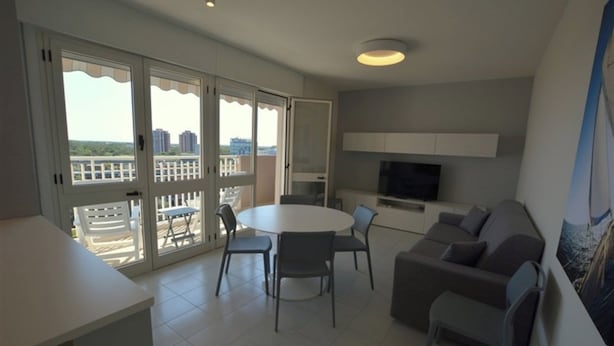 Een moderne woonkamer met een eethoek, een bank, een televisie en een balkon met uitzicht op gebouwen.