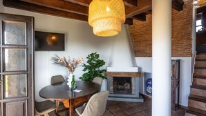 Un área de comedor con una mesa redonda, sillas, un florero con flores, una chimenea y una escalera.