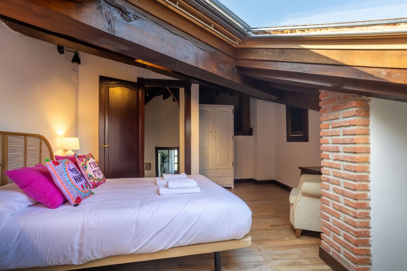 Een slaapkamer met een bed, kussens, een nachtkastje, een stoel en een dakraam.