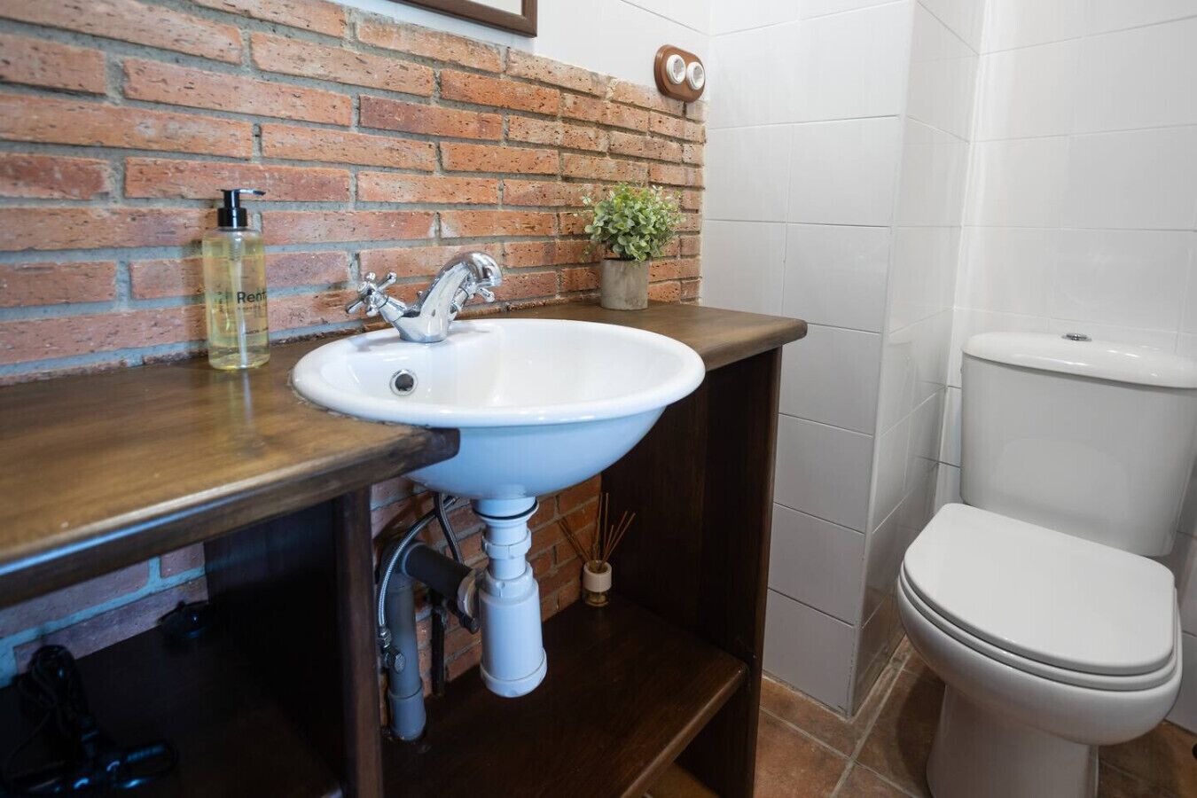 Een badkamer met een wit wastafel, een toilet en een bakstenen muur.