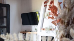 A room with a flat-screen TV on a wooden stand, a small plant on the stand, and a window with curtains. - Rural villa with sea views (Marianes)