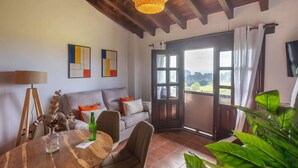 A cozy living room with a sofa, a dining table, and a large window with a view of the countryside.