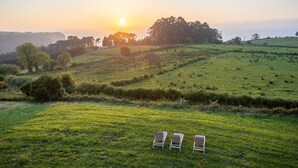 A grassy field with three white chairs and a sunset in the background.