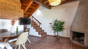 A spacious living area with a wooden staircase, a fireplace, a dining table with chairs, and a television mounted on the wall. - Infinite autumn in the Asturian coast with family (Marianes)