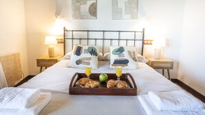 A hotel room with a neatly made bed, two bedside tables with lamps, a tray with croissants and juice, and abstract wall art. - Infinite autumn in the Asturian coast with family (Marianes)
