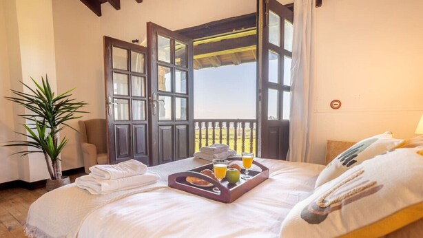 A hotel room with a bed, a tray with breakfast items, a chair, and a potted plant. - Infinite autumn in the Asturian coast with family (Marianes)