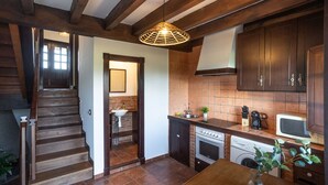 A kitchen with wooden beams, a staircase, a sink, a stove, and a microwave. - Infinite autumn in the Asturian coast with family (Marianes)