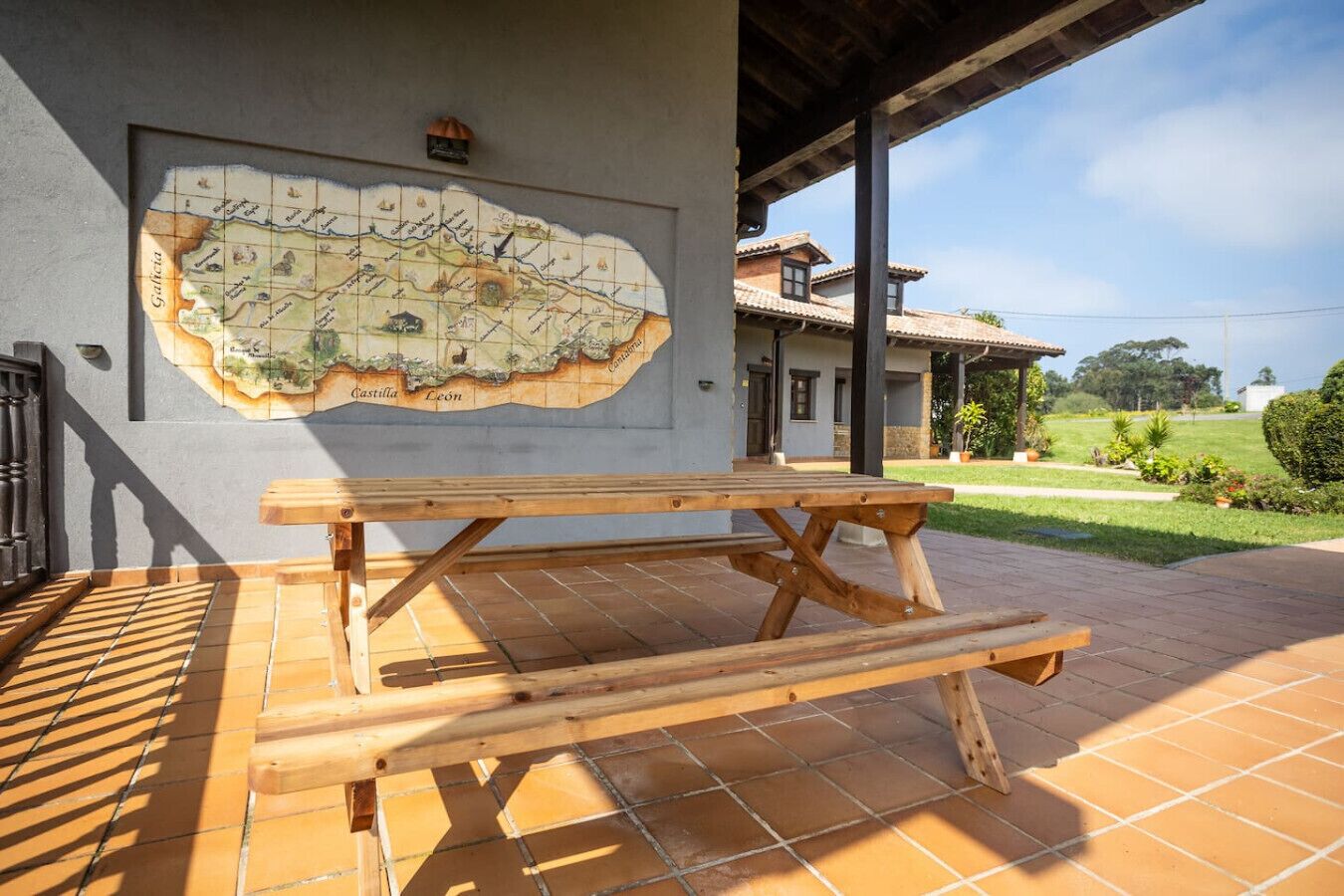 Een houten picknicktafel op een betegeld terras, met een kaart aan de muur.