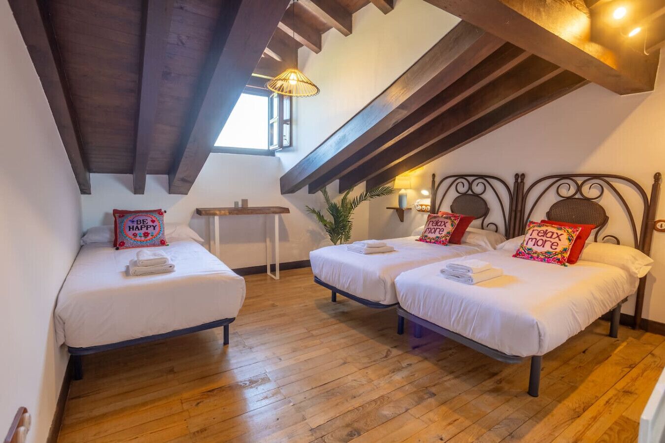 Un dormitorio abrigado en un ático con dos camas, vigas de madera, una mesita y un ventanal.