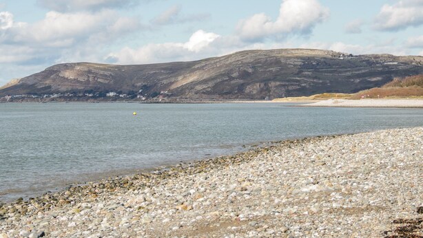 A pebbly beach with a calm sea, a distant hill, and a partly cloudy sky. - Flat 1A, Mona House (Conwy)