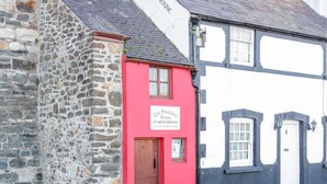 A stone building with a red door and a sign that reads "The Smallest House in Great Britain." - Flat 1A, Mona House (Conwy)