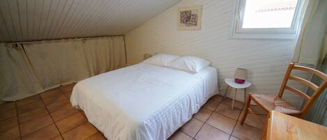 A bedroom with a bed, a chair, a small table, a window, and a picture on the wall.