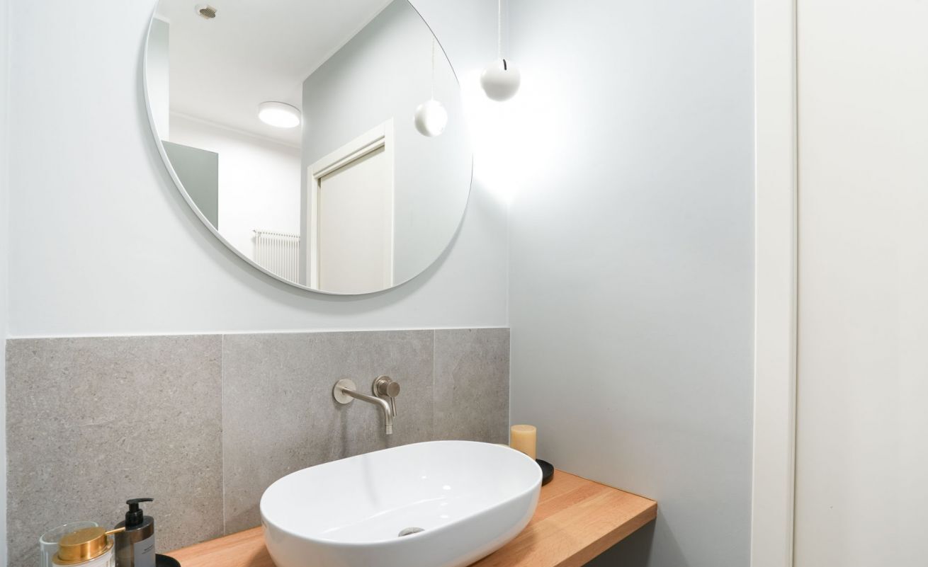 A bathroom with a round mirror, a white sink, and a wooden countertop.