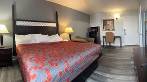 Habitación de hotel con una cama grande, un escritorio, una silla, un televisor y una puerta que da a otra habitación.