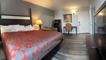 A hotel room with a large bed, a desk, a chair, a TV, and a door leading to another room.