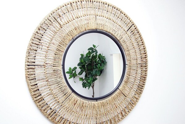 A circular woven mirror with a central reflective surface and a plant in the middle.