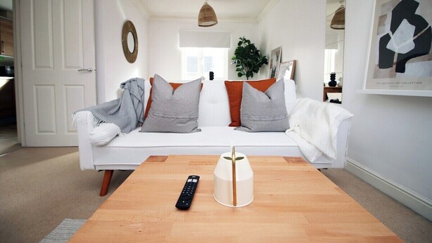A modern living room with a white sofa, a wooden coffee table, and a remote control.