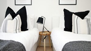 A bedroom with two beds, each with black and white striped bedding, a small bedside table with a lamp, and abstract art on the wall.