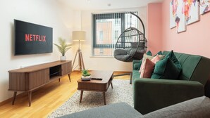 A modern living room with a TV, sofa, coffee table, lamp, hanging chair, and artwork on the wall.
