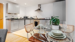 A modern kitchen with grey cabinets, a stainless steel range hood, and a dining area with a round table set for two.