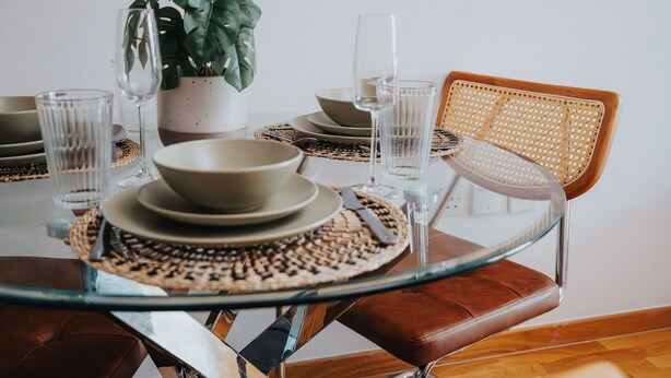 A dining table with a glass top, surrounded by chairs, plates, bowls, and cutlery.