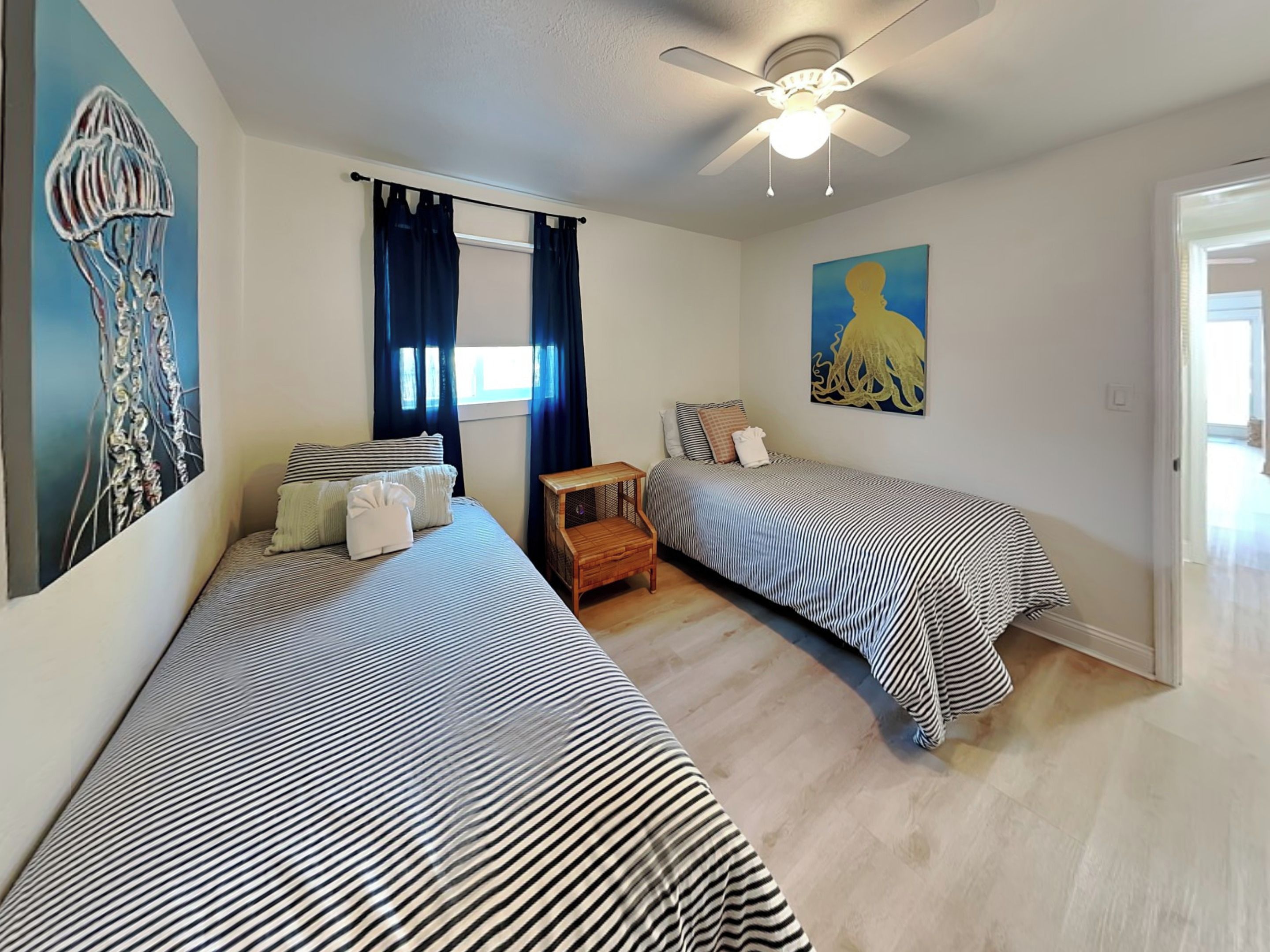 Une chambre avec deux lits, un ventilateur de plafond et des œuvres d’art accrochées aux murs.