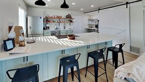 Eine moderne Küche mit einer großen Kochinsel, Barhocker, Pendelleuchten und einer Schiebetür im Bauernhausstil.