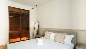A modern hotel room with a large bed, a wooden wardrobe, and a bedside table.
