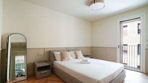 Un dormitorio con una cama grande, mesitas de noche, un espejo y un ventanal corredero al exterior.