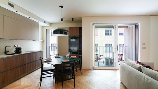 Una cocina moderna con comedor, un sofá y un ventanal corredera que da a un balcón exterior.