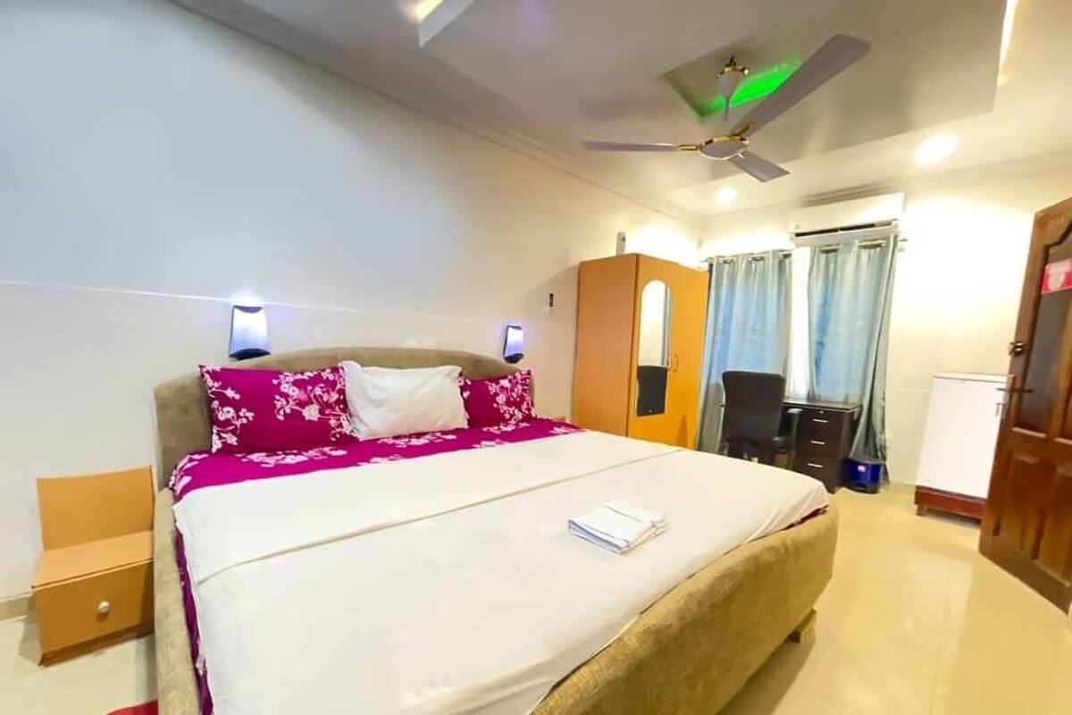 Une chambre d’hôtel comprenant un lit, un ventilateur de plafond, une armoire, un bureau et une chaise.