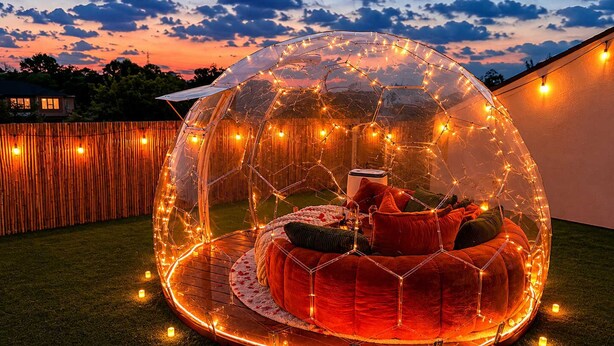 Une structure en forme de dôme transparent, avec un espace de sièges circulaire à l’intérieur, le tout illuminé par des guirlandes lumineuses.