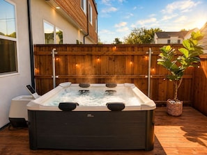 A hot tub in a wooden deck area with a wooden fence and a potted plant.