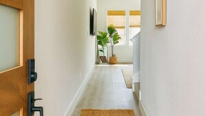 Un couloir avec une porte en bois, un tapis tissé et une plante.