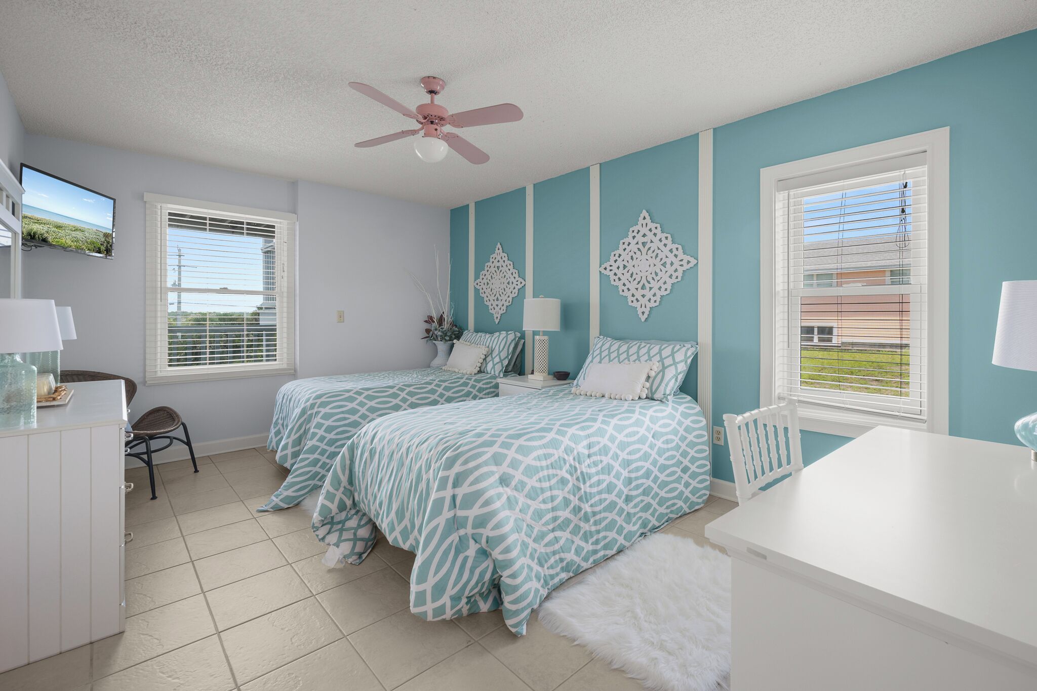 A bedroom with two beds, a ceiling fan, and a window with blinds.