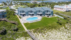 A large, two-story house with a swimming pool, surrounded by a well-maintained lawn and palm trees. - Ocean Eight 101 by Distinctive Beach Rentals (St. Augustine)