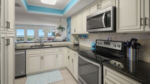 A kitchen with white cabinets, a black stove, and a microwave. - Ocean Eight 101 by Distinctive Beach Rentals (St. Augustine)