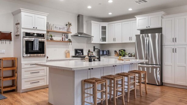 A modern kitchen with white cabinetry, stainless steel appliances, a large island with stools, and a wooden bar stool. - Escondido Oasis | Sleeps 10 + Hot Tub! (Escondido)