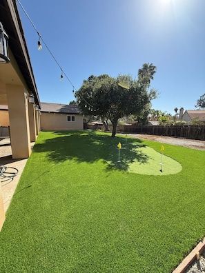 A backyard with artificial grass, a tree, and a golf hole. - Escondido Oasis | Sleeps 10 + Hot Tub! (Escondido)