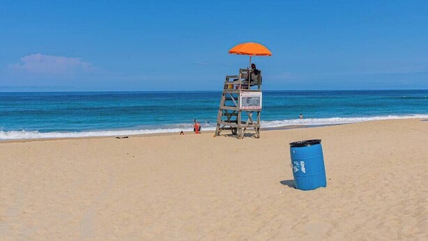 A lifeguard tower with an orange umbrella on a sandy beach. - Counting Pelicans + Ocean View + Pelican Hunt (Kill Devil Hills)