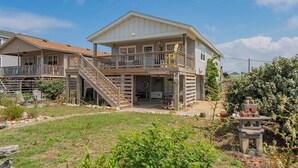 A two-story house with a balcony, a front porch, and a small garden area. - Counting Pelicans + Ocean View + Pelican Hunt (Kill Devil Hills)