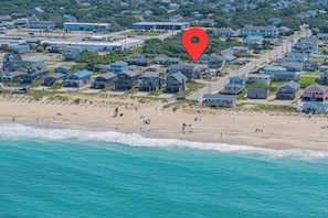 An aerial view of a coastal residential area with houses, a beach, and a lifeguard tower. - Counting Pelicans + Ocean View + Pelican Hunt (Kill Devil Hills)