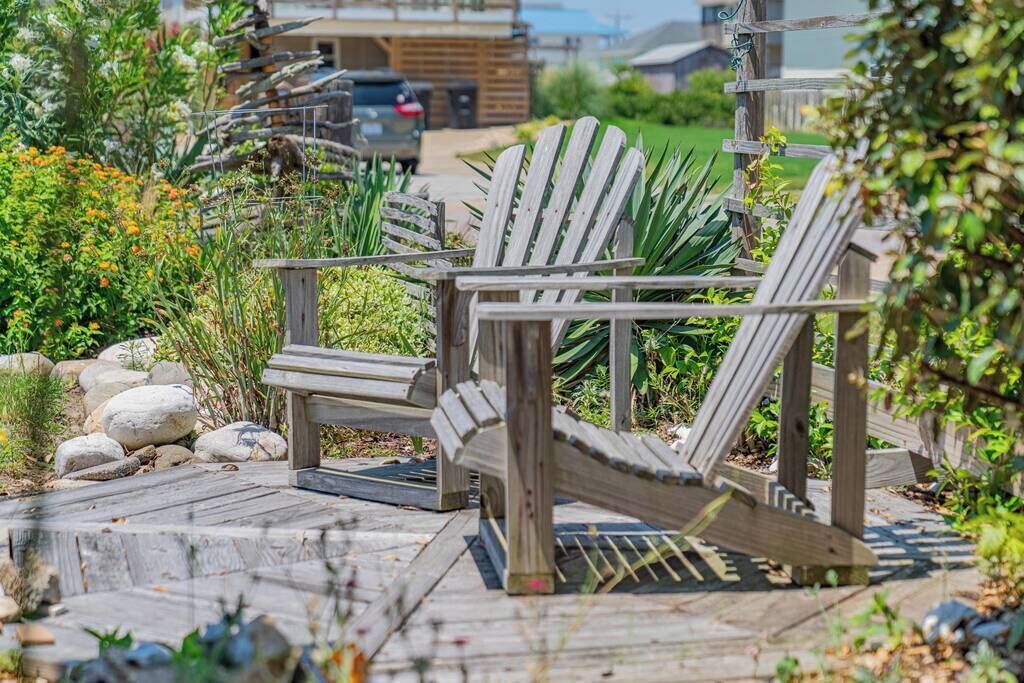 Eine Holzterrasse mit Adirondack-Stühlen, umgeben von einem Garten mit Steinen und Pflanzen.